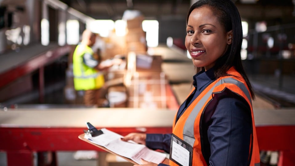 warehouse manager holding a clipboard with workers in the background