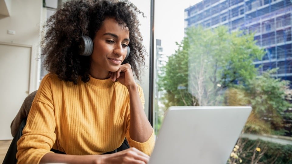 woman watching the latest webinar on a laptop with headphones